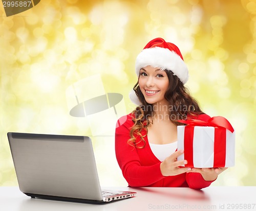 Image of smiling woman in santa hat with gift and laptop