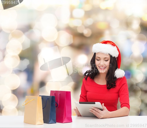 Image of smiling woman in santa hat with bags and tablet pc