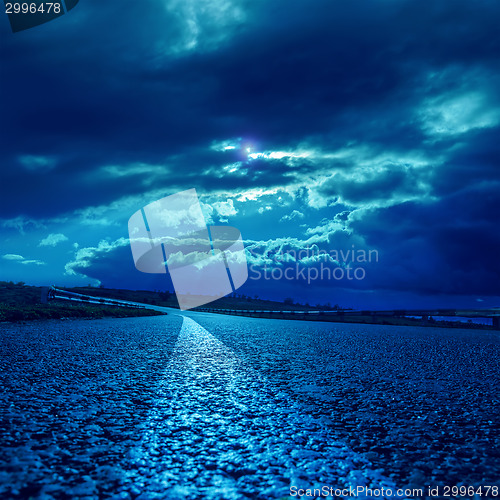 Image of low dramatic clouds over asphalt road in dark blue moonlight