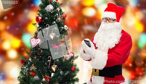 Image of santa claus with smartphone and christmas tree