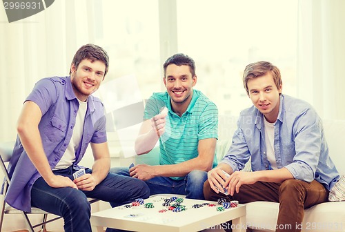 Image of happy three male friends playing poker at home