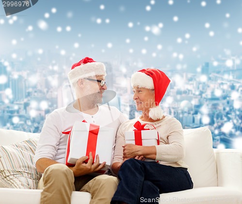 Image of happy senior couple in santa hats with gift boxes