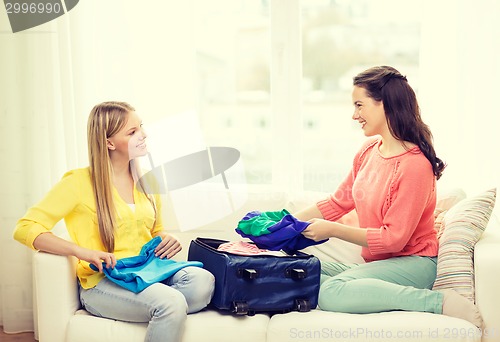 Image of two smiling teenage girls packing suitcase at home