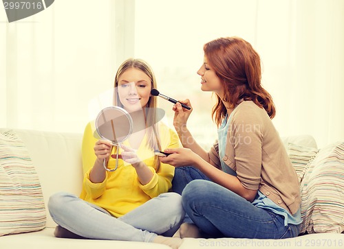 Image of two smiling teenage girls applying make up at home