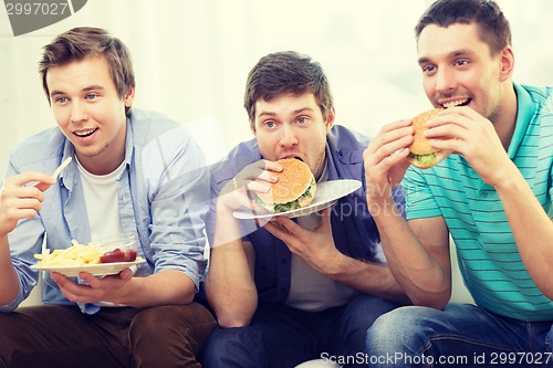 Image of smiling friends with soda and hamburgers at home