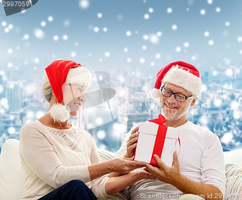 Image of happy senior couple in santa hats with gift box