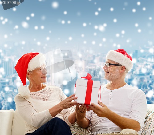 Image of happy senior couple in santa hats with gift box