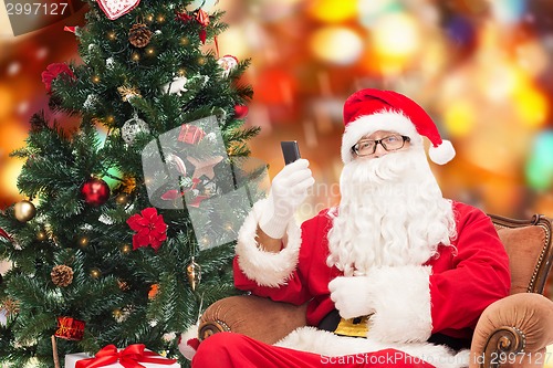 Image of santa claus with smartphone and christmas tree