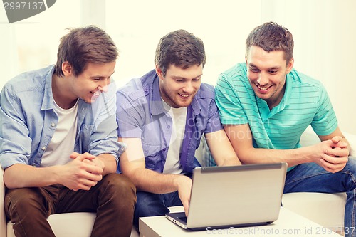 Image of smiling friends with laptop computer at home