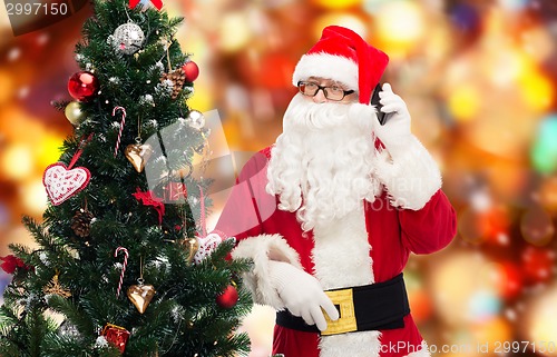 Image of santa claus with smartphone and christmas tree