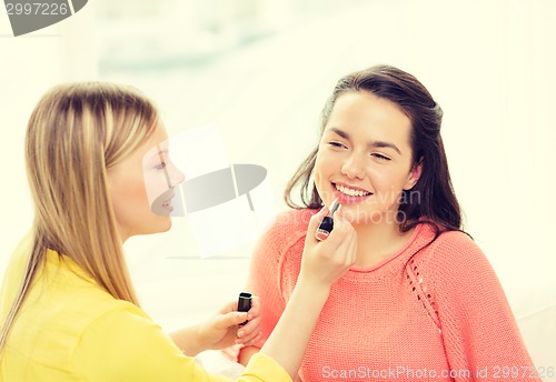 Image of two smiling teenage girls applying make up at home