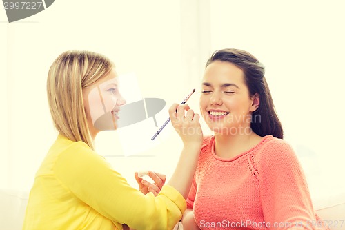 Image of two smiling teenage girls applying make up at home