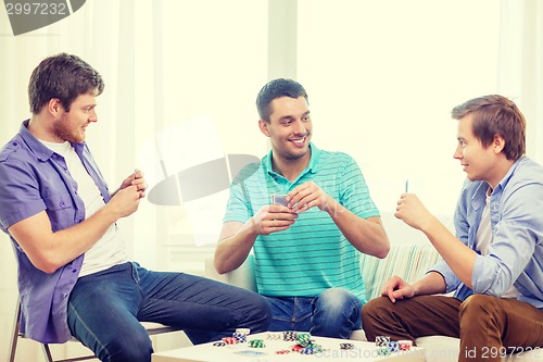 Image of happy three male friends playing poker at home