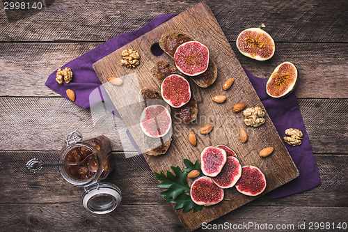 Image of Sliced figs, nuts and bread with jam on choppingboard in rustic 