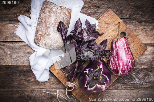 Image of Aubergines, basil and bread on chopping board and wood