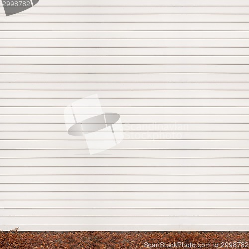 Image of wooden plank wall, ground covered with fallen leaves