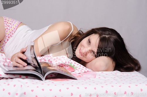 Image of girl thumbs through a magazine while lying in bed