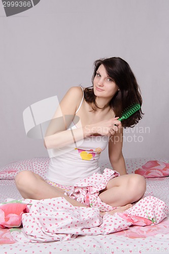 Image of Girl combing her hair sitting in bed