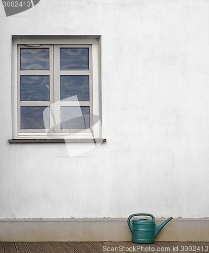 Image of plastic watering can near the white wall