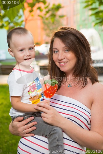 Image of Laughing young pregnant mother playing with her son in a beautiful garden