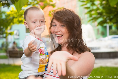Image of Laughing young pregnant mother playing with her son in a beautiful garden