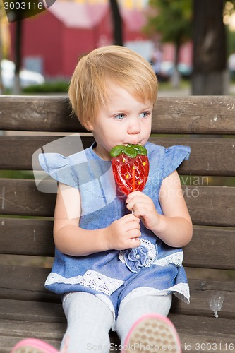 Image of Beautiful little girl holding strawberry shaped lollipop
