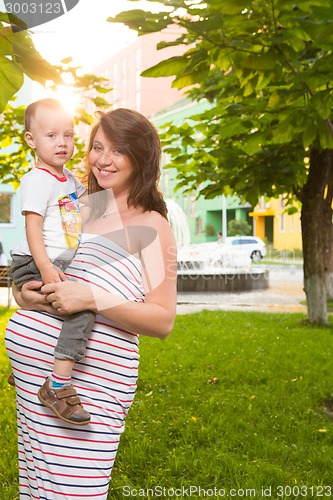 Image of Laughing young pregnant mother playing with her son in a beautiful garden