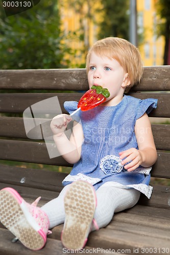 Image of Beautiful little girl holding strawberry shaped lollipop