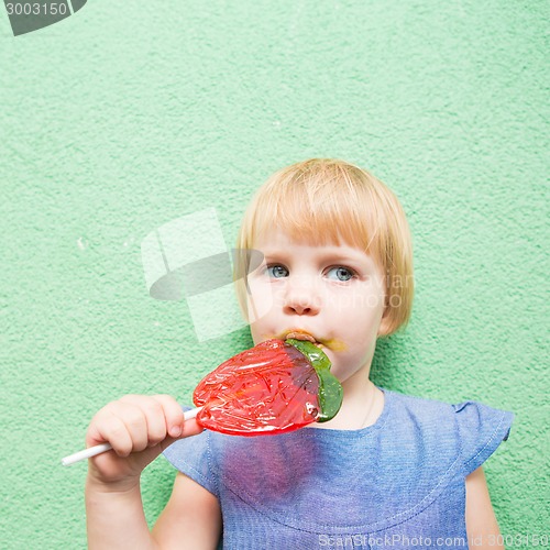 Image of Beautiful little girl holding strawberry shaped lollipop