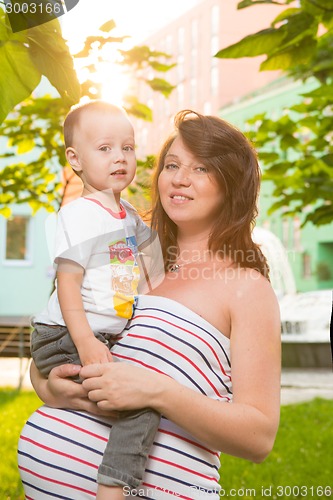 Image of Laughing young pregnant mother playing with her son in a beautiful garden