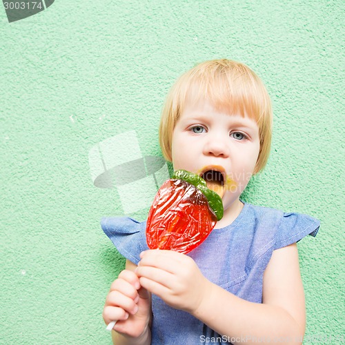 Image of Beautiful little girl holding strawberry shaped lollipop