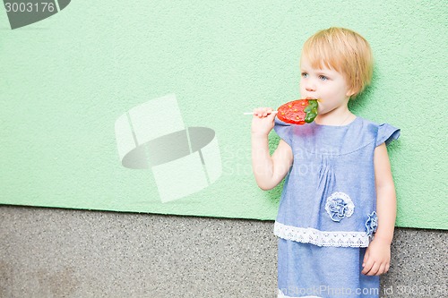 Image of Beautiful little girl holding strawberry shaped lollipop