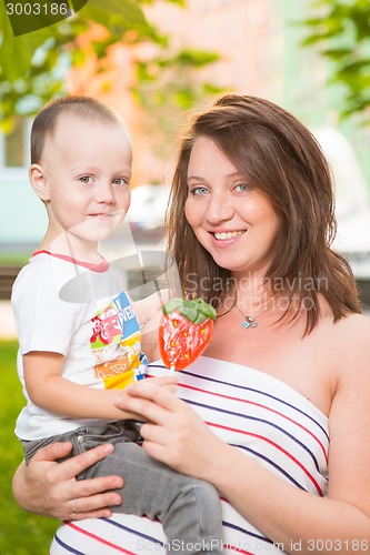 Image of Laughing young pregnant mother playing with her son in a beautiful garden