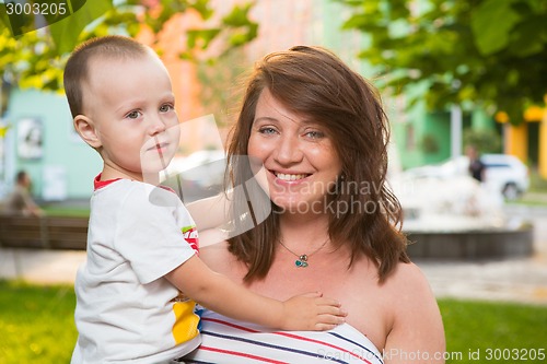 Image of Laughing young pregnant mother playing with her son in a beautiful garden