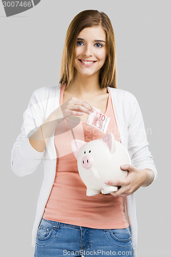 Image of Beautiful woman putting money in a piggy bank