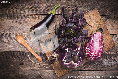 Image of Aubergines, basil and spoon on chopping board and wooden table