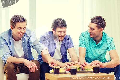 Image of smiling friends with soda and hamburgers at home