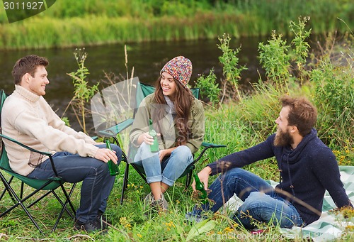 Image of group of smiling tourists drinking beer in camping