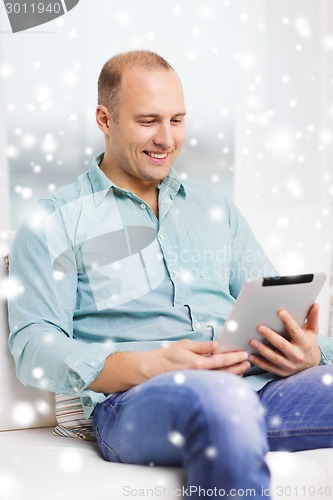 Image of smiling man with tablet pc sitting on couch