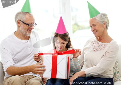 Image of smiling family in party hats with gift box at home