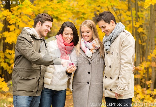 Image of smiling friends with smartphones in city park