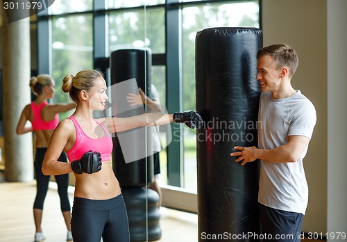 Image of smiling woman with personal trainer boxing in gym