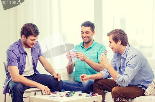 Image of happy three male friends playing poker at home