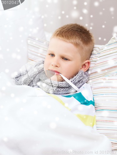 Image of ill boy with thermometer lying in bed at home