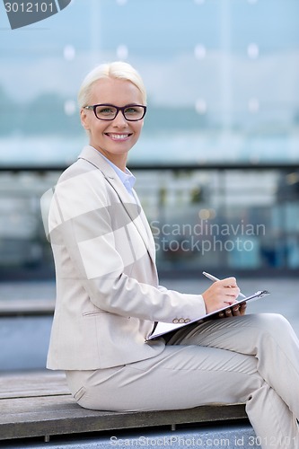 Image of young smiling businesswoman with notepad outdoors