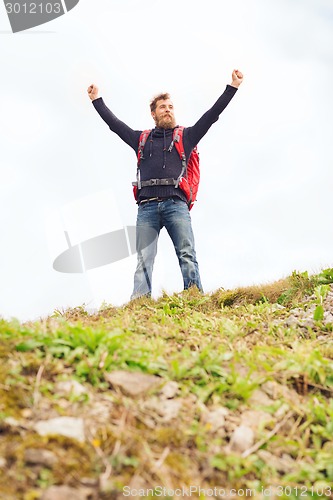 Image of tourist with beard and backpack raising hands