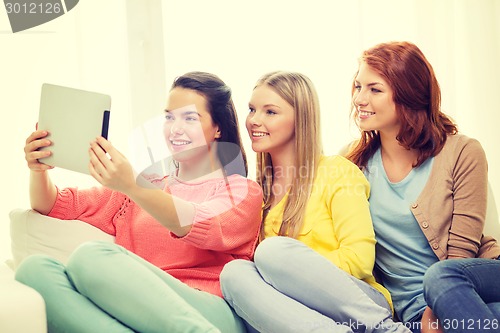 Image of three smiling teenage girls with tablet pc at home