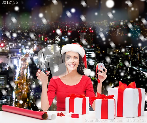 Image of smiling woman in santa helper hat packing gifts
