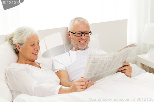 Image of happy senior couple with newspaper in bed