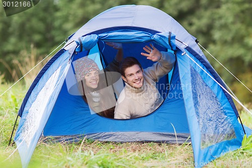 Image of smiling couple of tourists looking out from tent